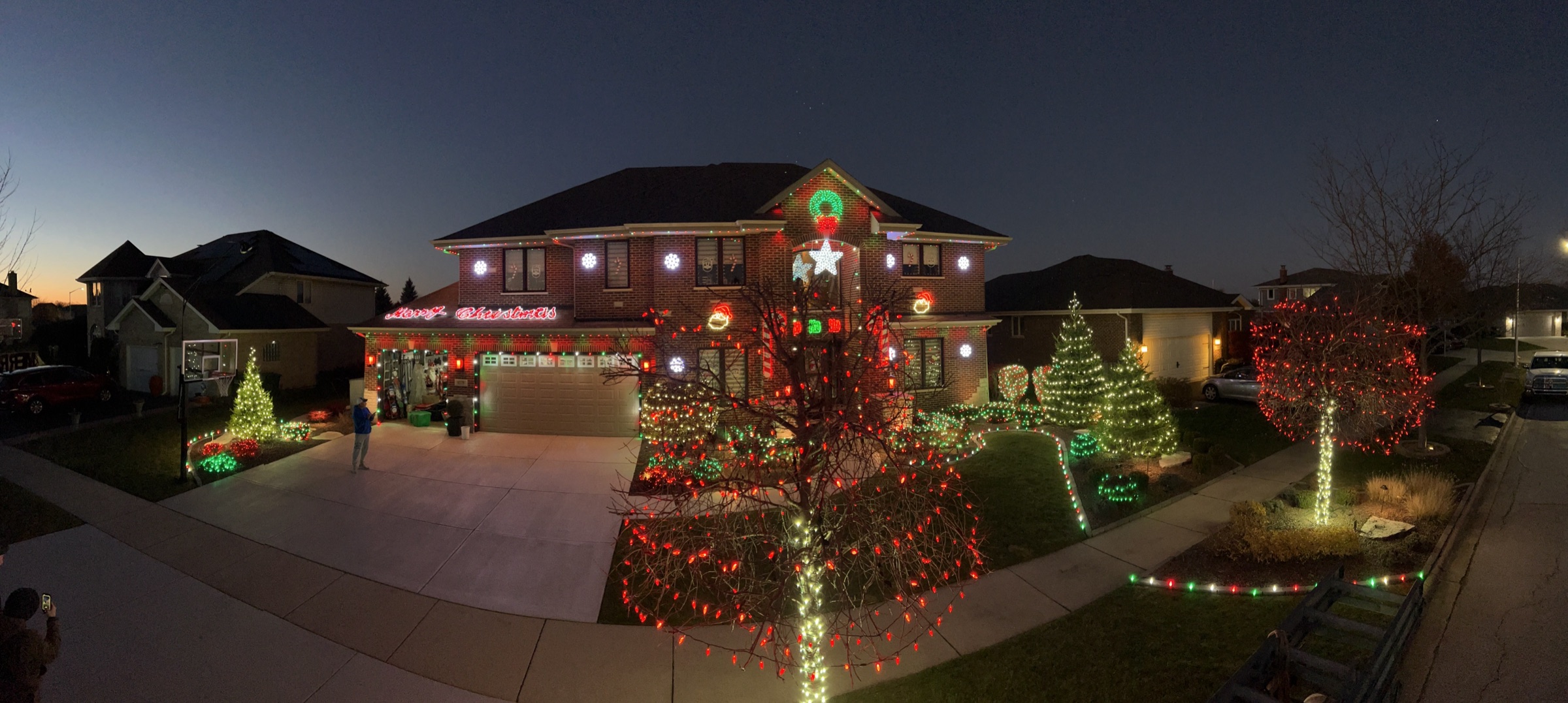 Panoramic view of a fully lit home and yard, trees and bushes all decorated